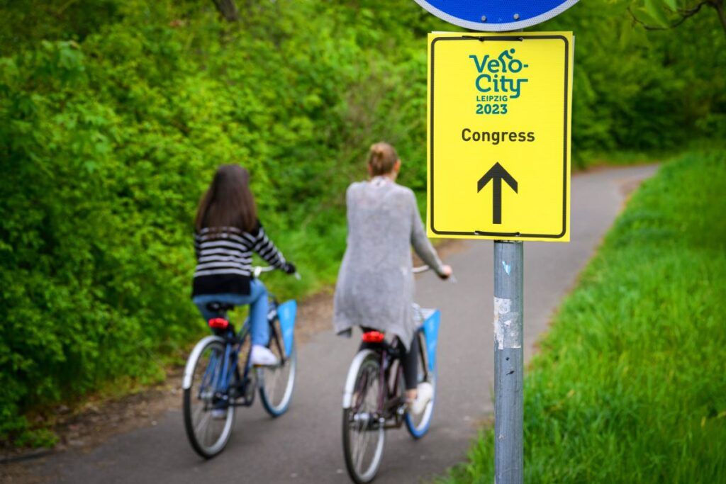 2 Personen mit Fahrrad auf Radweg und Velo-City-Schild