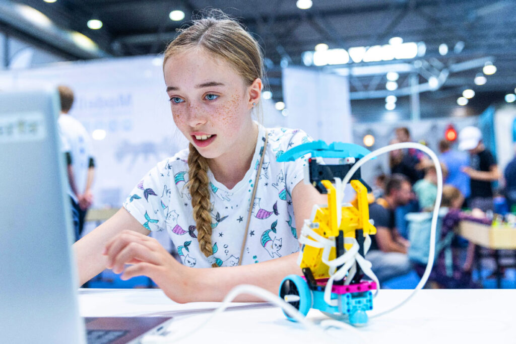 Ein Mädchen vor einem Laptop programmiert auf der Hobbymesse Leipzig einen Spielzeug-Roboter.