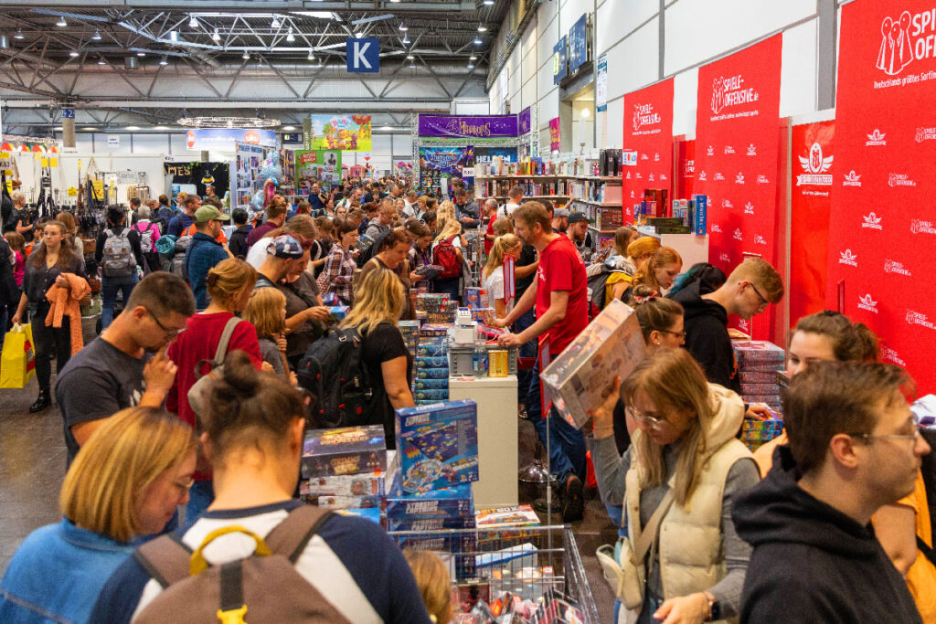 Besucher der Hobbymesse Leipzig kaufen Spiele in einem Messestand.
