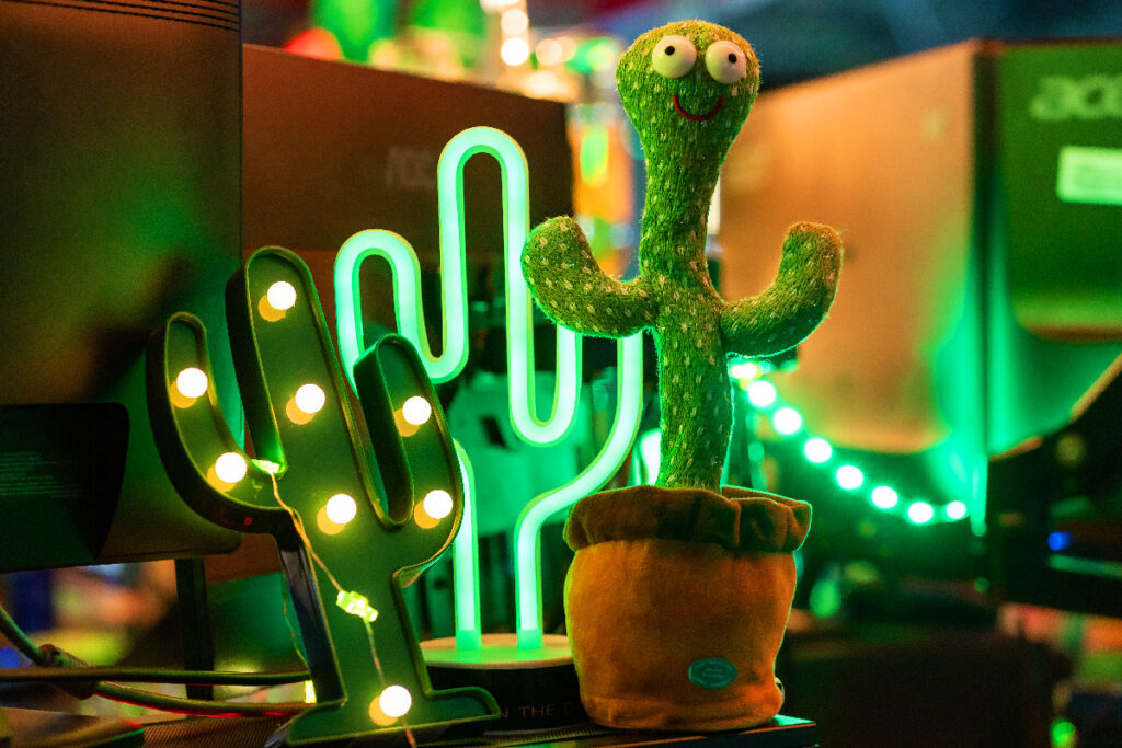 Foto von einem Plüschkaktus und Lampen in Kaktus-Form neben Gaming-Equipment bei der CAGGTUS 2023.